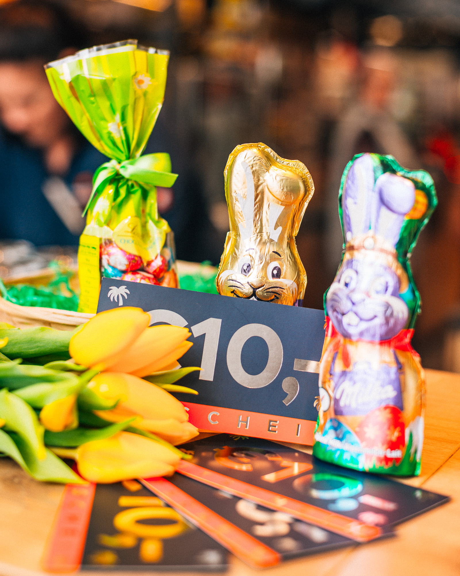 Gutscheine sind neben Schokoosterhasen, Blumen und Pralinen am Tisch platziert.