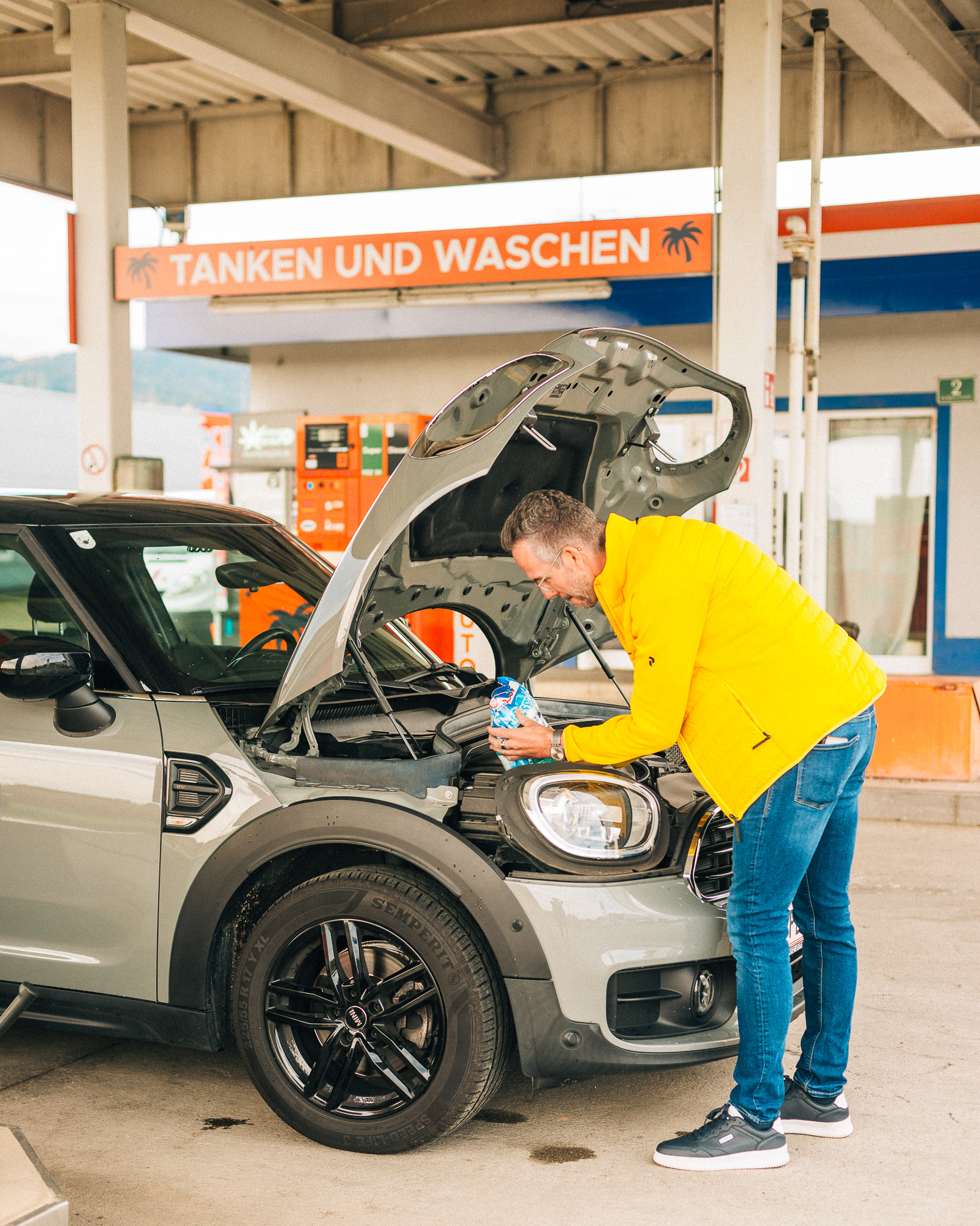 Mann füllt Scheibenfrostschutz beim Auto nach.